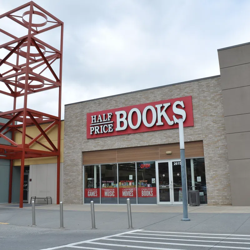Half Price Books store exterior with large red and white sign and metal architectural feature against a cloudy sky.
