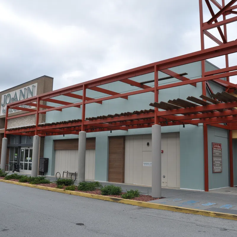 Exterior view of a shopping center with Jo-Ann fabric store and covered walkway with red metal framework.