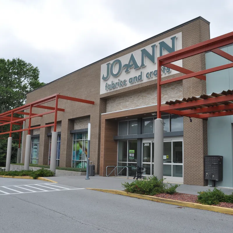Exterior view of JOANN fabrics and crafts store with brick facade and red pergola on a cloudy day