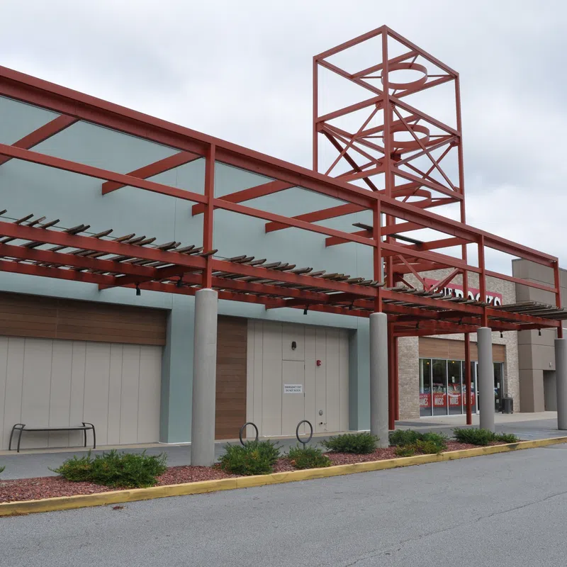 Empty shopping center front with red metal framework and closed store entrances under cloudy sky