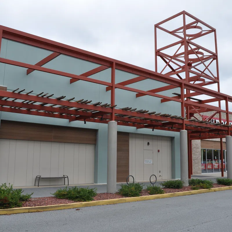 Empty storefront with modern red metal awning structure and overcast sky in a shopping center parking lot