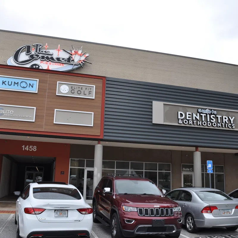 Exterior of a commercial building with signs for Kumon, Elite Golf, dentistry, and parked cars outside