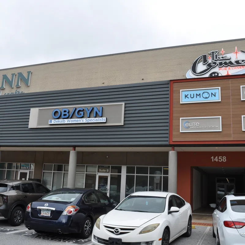 Shopping plaza exterior with storefronts including JOANN, OB/GYN, Kumon, and parking lot with cars in front.