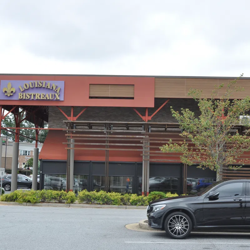 Louisiana Bistreaux restaurant exterior with a parked black car and surrounding greenery in a shopping area.