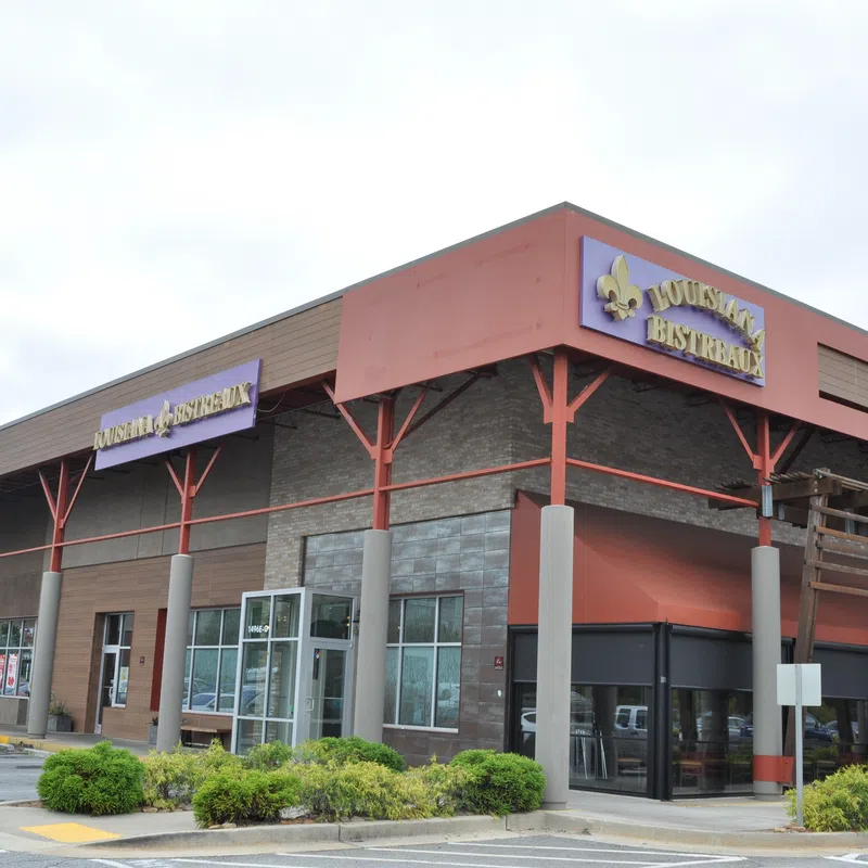 Corner view of a shopping plaza with Louisiana Bistreaux restaurant and various stores under a cloudy sky.