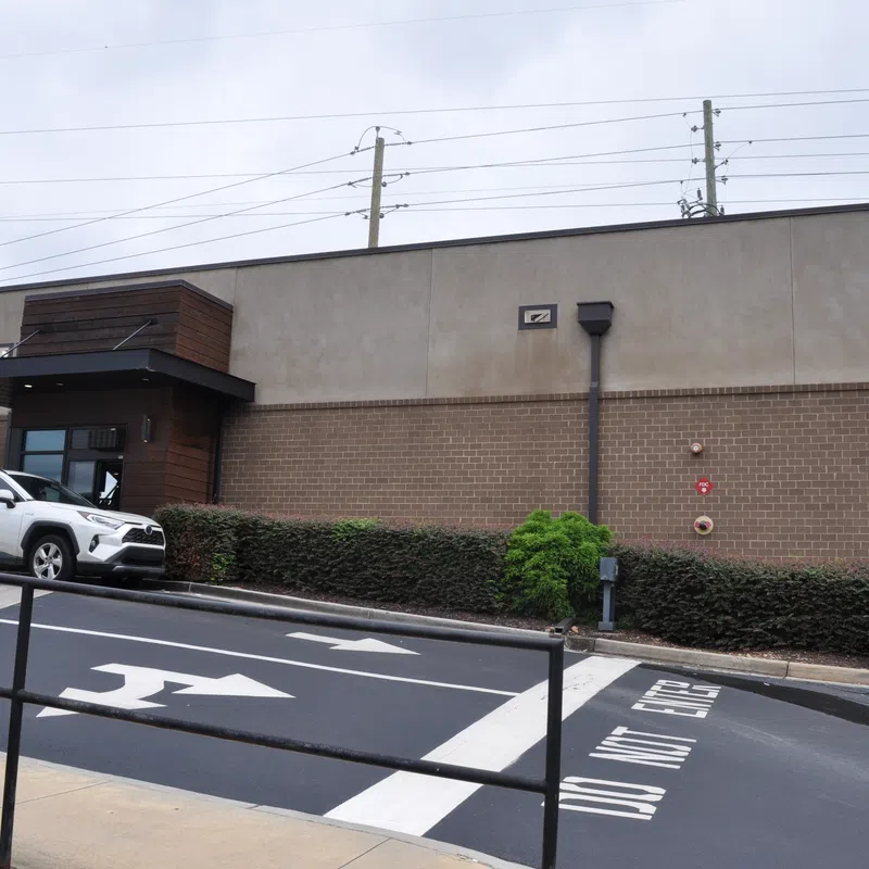 Exterior view of a Starbucks coffee shop with a white SUV parked and directional arrows on the road.