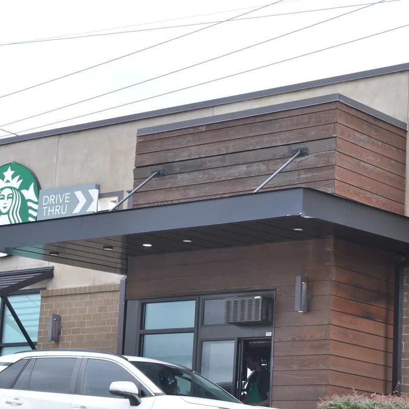 Starbucks coffee shop exterior with drive-thru lane and a white SUV parked nearby during daytime.