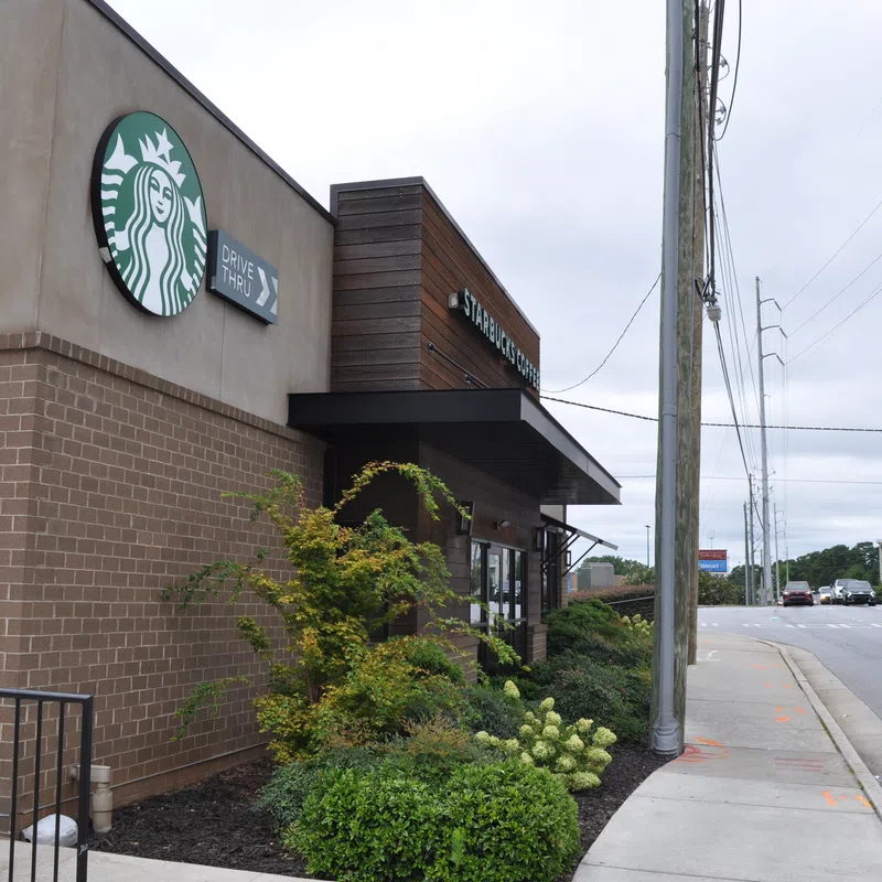 Exterior view of a Starbucks coffee shop with drive-thru signs and a nearby street intersection on a cloudy day