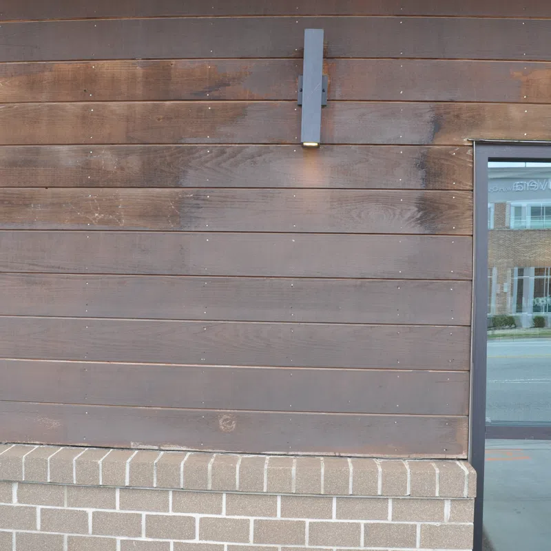 Wood-paneled wall with modern light fixture above brick ledge next to reflective glass window showing street view.