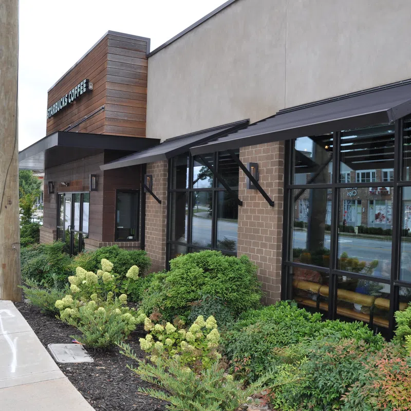 Starbucks Coffee shop exterior with large windows, awnings, and landscaped greenery along the sidewalk.