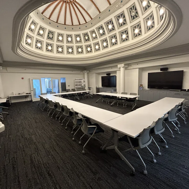 Conference room with U-shaped tables and chairs under a decorative domed ceiling with natural light.