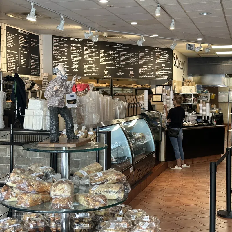 Cozy bakery interior with bread display, glass cases, menu boards, and customer ordering at counter.