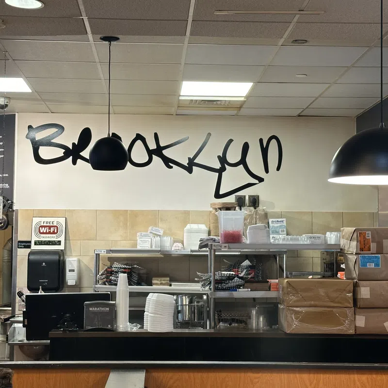 Interior of a Brooklyn restaurant with shelves, stacked boxes, pendant lights, and handwritten wall text.