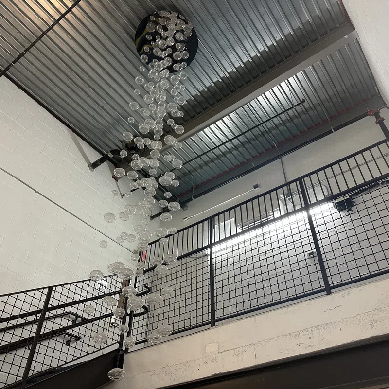 Modern indoor stairwell with metal railings and hanging glass bubble chandelier under industrial ceiling.