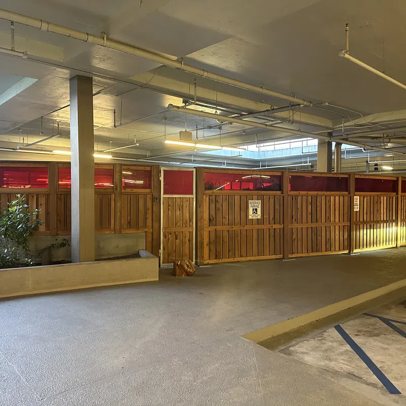 Indoor parking area with wooden privacy partitions and red-tinted upper panels under fluorescent lights
