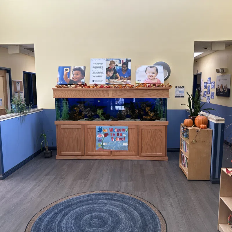 School lobby with large aquarium, welcome sign, children's artwork, bookshelves, and autumn decorations including pumpkins.