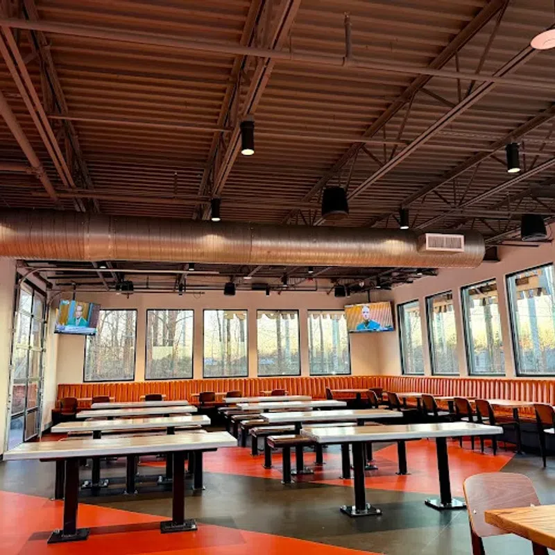Spacious restaurant dining area with orange booths, wooden tables, black chairs, and large windows with outdoor views.