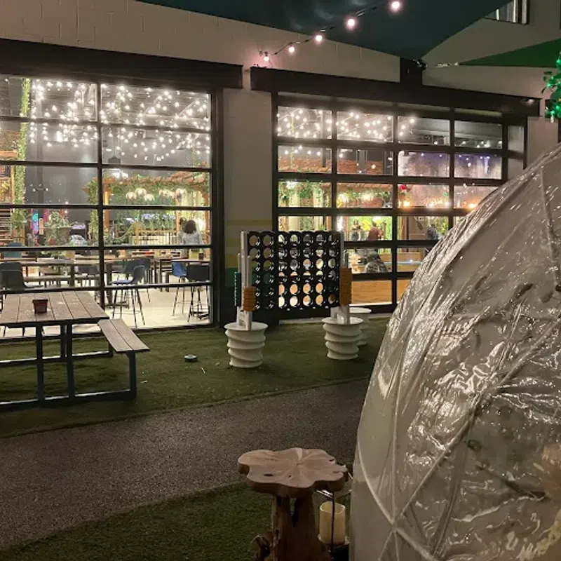Outdoor dining area with picnic table, clear igloo dome, oversized Connect Four game, and string lights at night