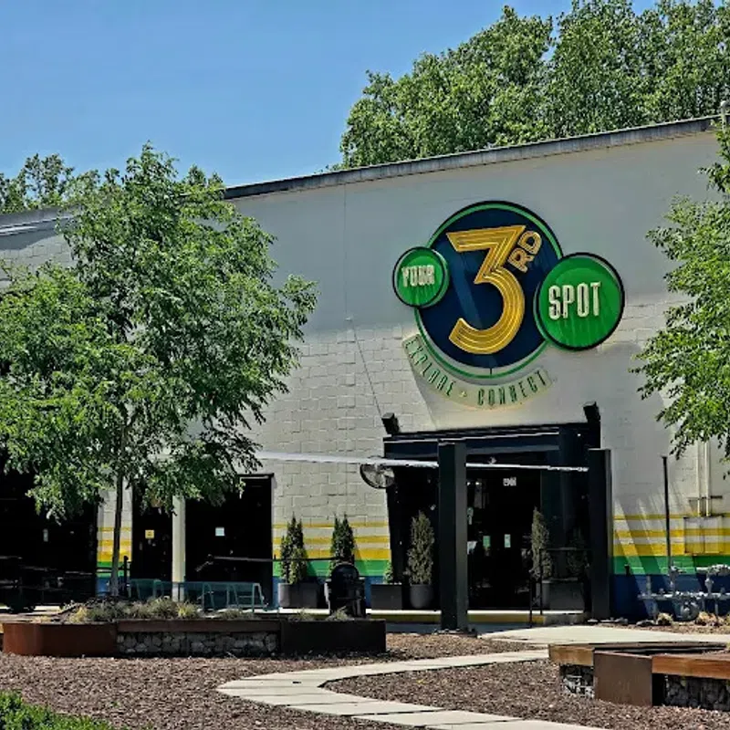 Exterior of a building with a large colorful 3rd Spot logo, surrounded by trees and outdoor seating area.