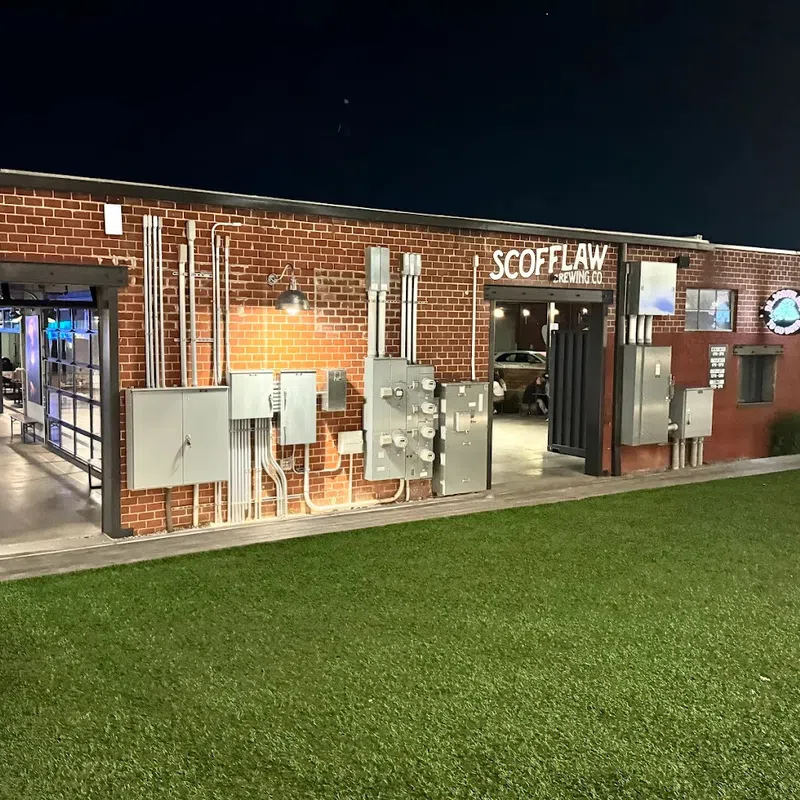 Night view of Scofflaw Brewing Co building with exposed brick, electrical panels, and green lawn in front.
