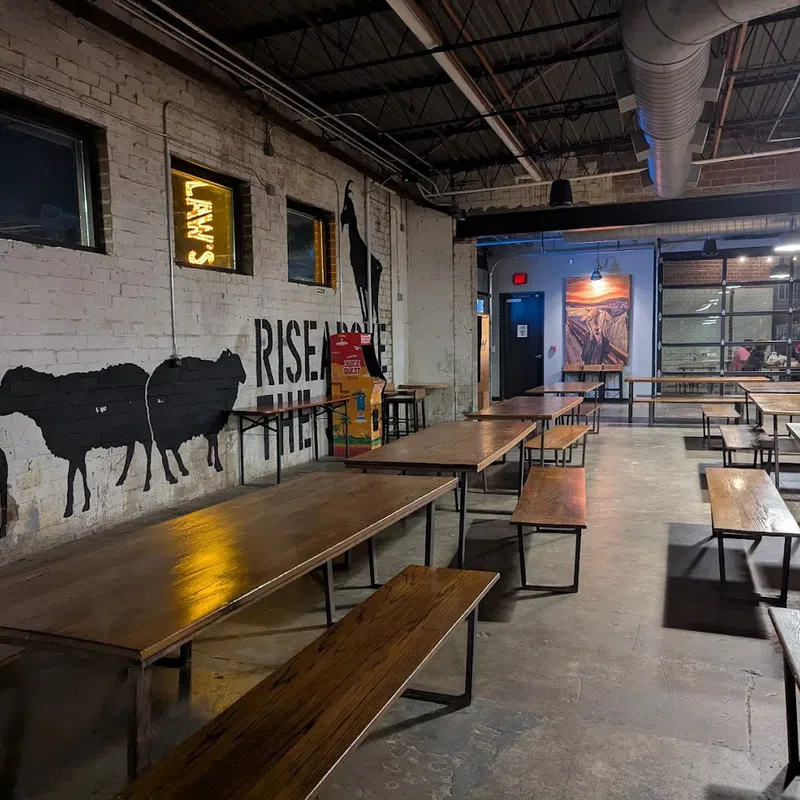 Interior of a rustic industrial dining area with wooden tables, benches, and animal murals on brick walls.