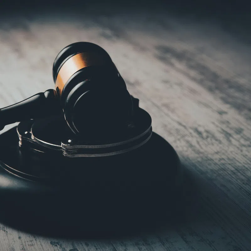 Wooden judge gavel and sound block on textured dark wooden table symbolizing law and justice.