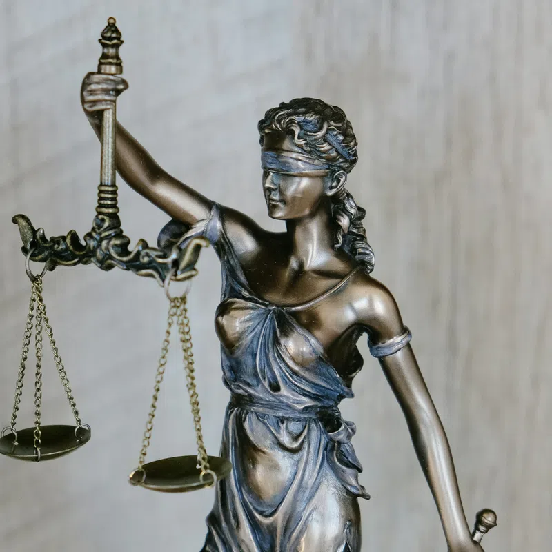 Bronze statue of Lady Justice blindfolded holding balanced scales against a wood background.