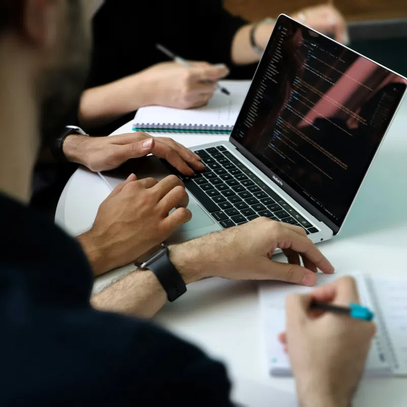 Team of developers collaborating with code on laptop and taking notes during a meeting.