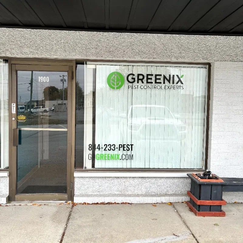 Storefront of Greenix Pest Control experts with logo, phone number, and website on window blinds at 1900 address.