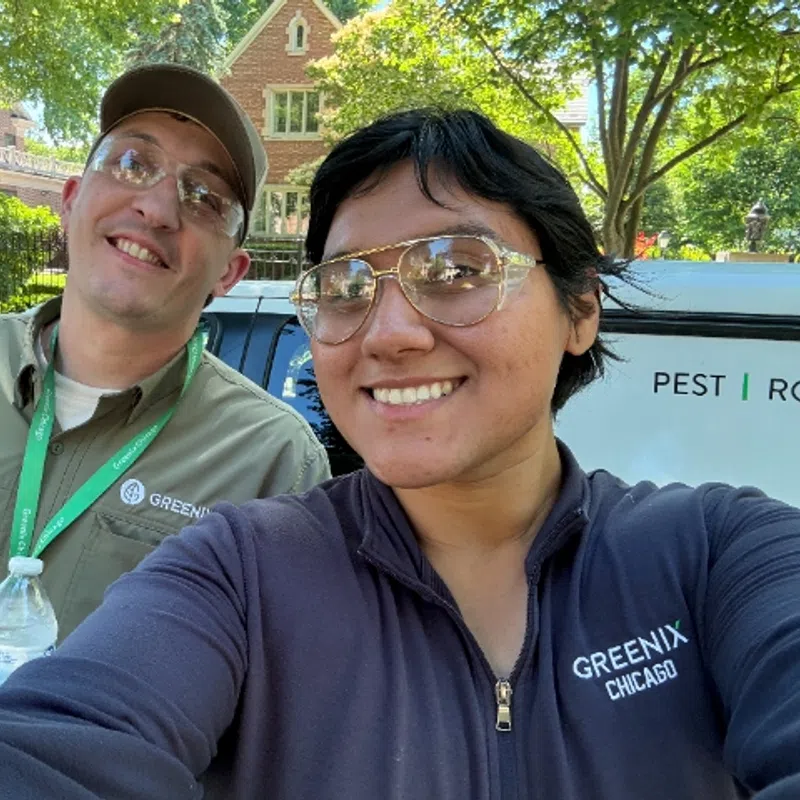 Two smiling Greenix Chicago pest control workers taking a selfie outdoors in front of a company van.