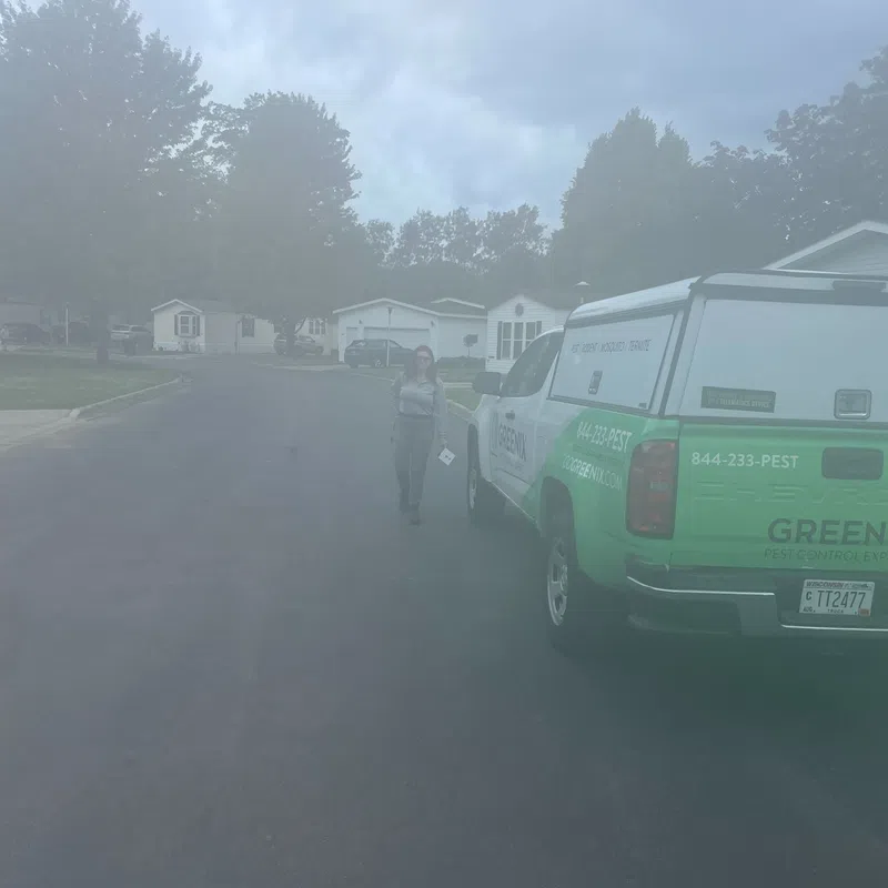 Technician walking toward a green pest control service truck in a suburban neighborhood on an overcast day