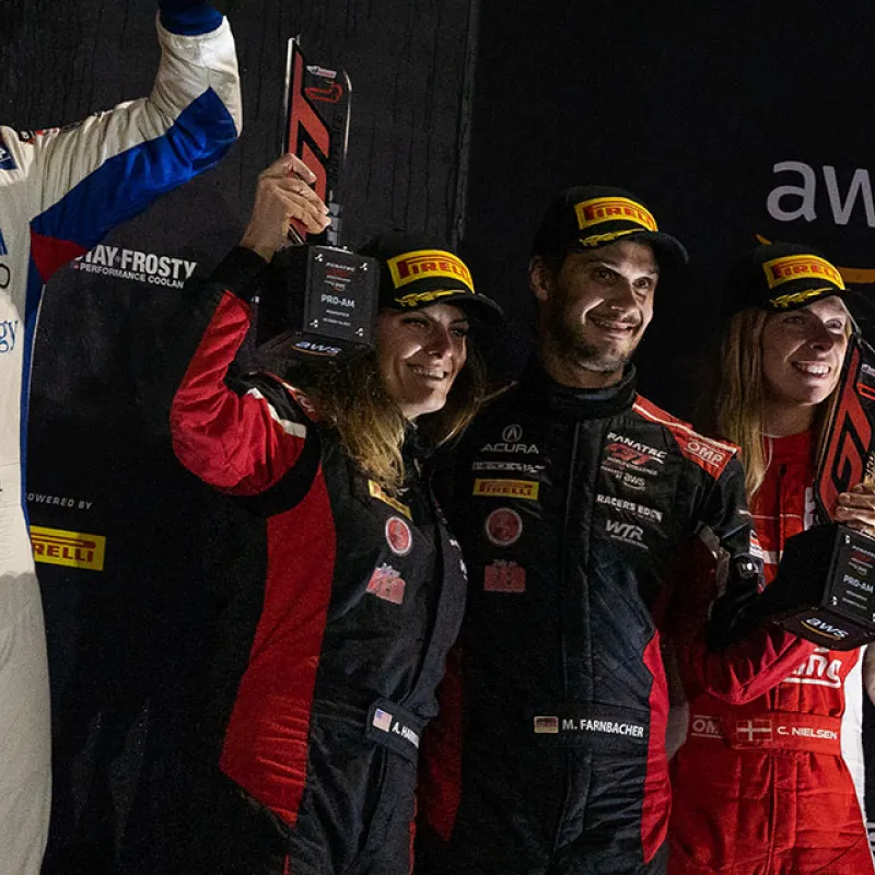 Race car drivers in racing suits hold trophies and celebrate on the podium after a Pirelli GT3 race victory.
