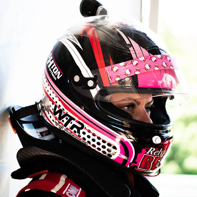 Side profile of a race car driver wearing a black and pink helmet with Hello Kitty decals and racing suit.