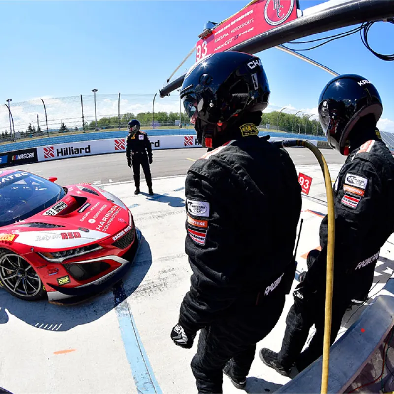Race car number 93 in red and white at pit stop with crew in black suits and helmets during sunny day