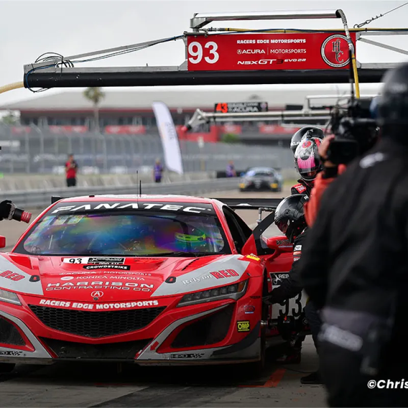 Red Acura NSX GT3 race car 93 in pit stop with crew members during motorsports event