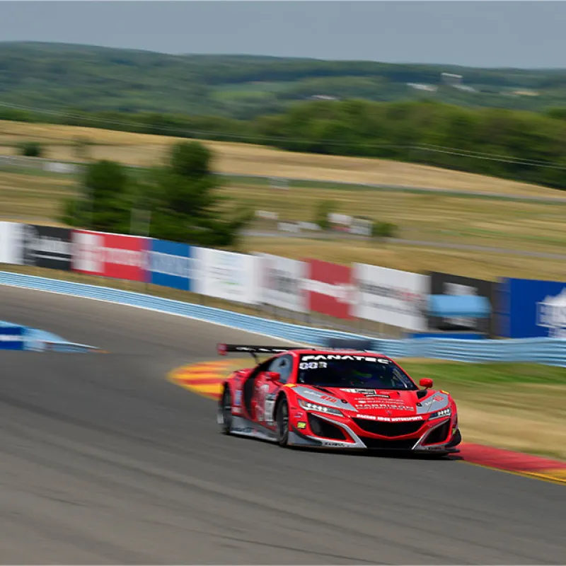 Red race car speeding on a curving racetrack with advertising banners and trees in background
