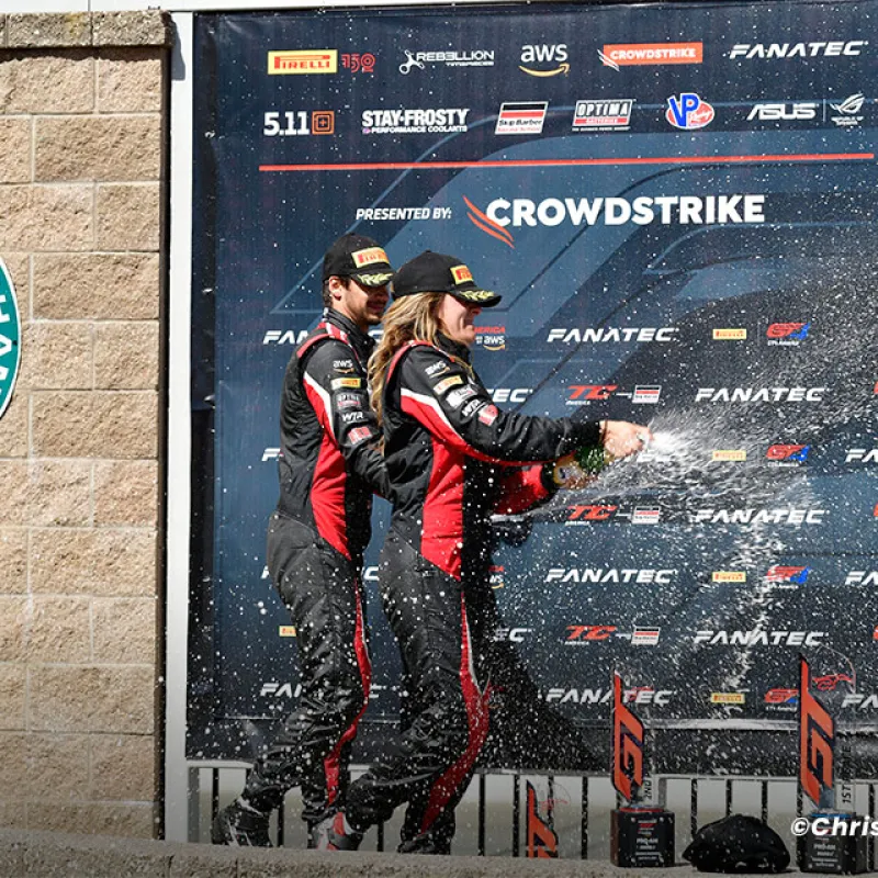 Race car drivers celebrate with champagne spray on podium after Korbel Champagne GT World Challenge event.