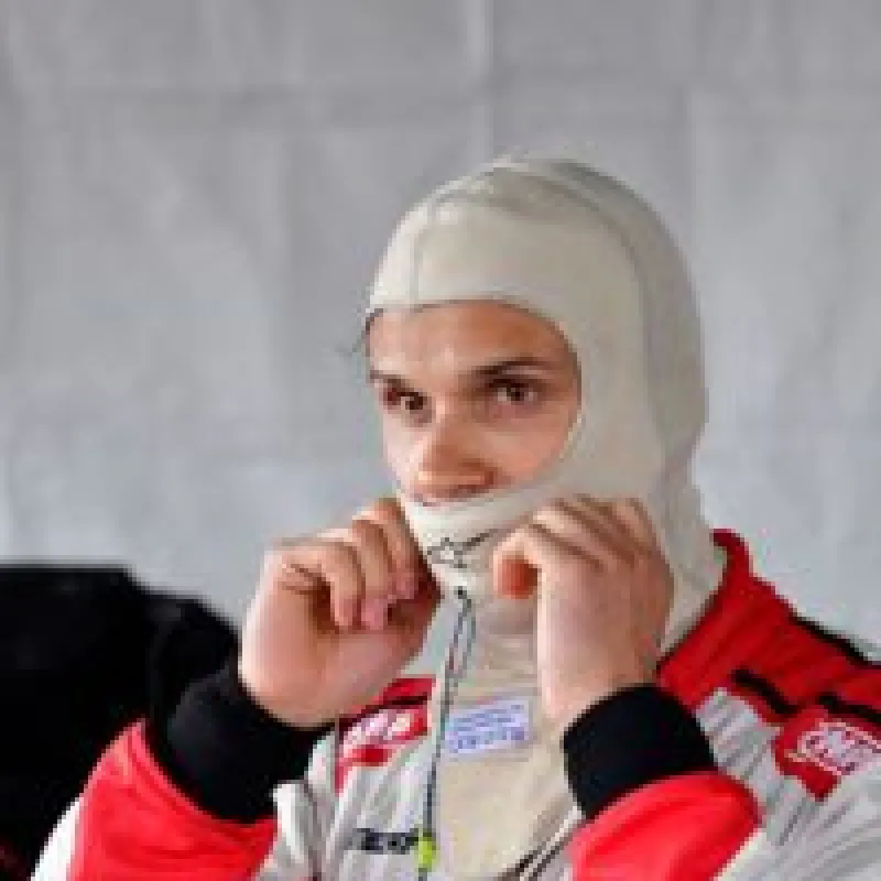 Race car driver adjusting white helmet liner, wearing white and red motorsport racing suit indoors.