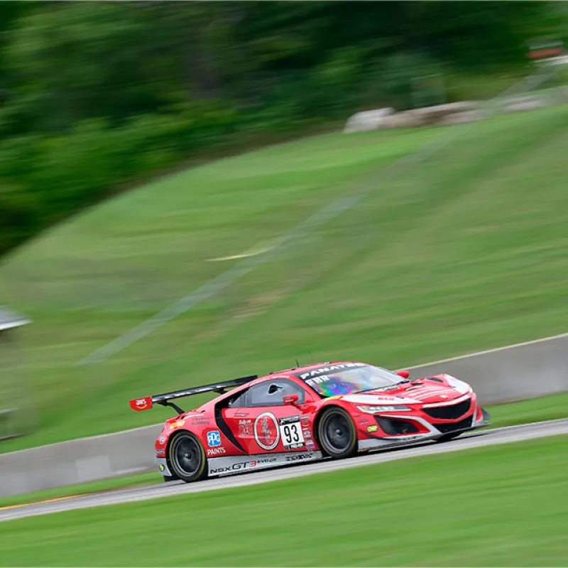 Red race car number 93 speeding on a racetrack with blurred green background and motion effect