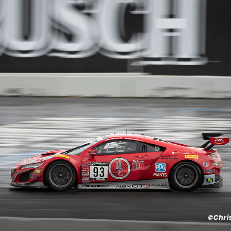 Red NSX GT3 EVO race car number 93 speeding on race track with sponsor logos and blurred background.