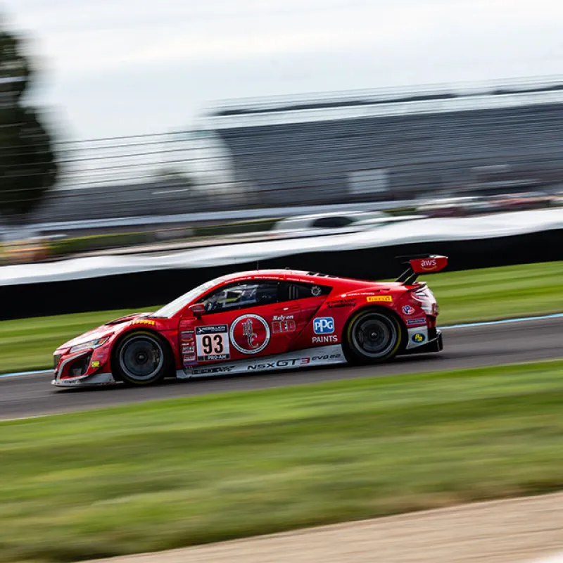 Red race car number 93 speeding on a racetrack with blurred background and green grass