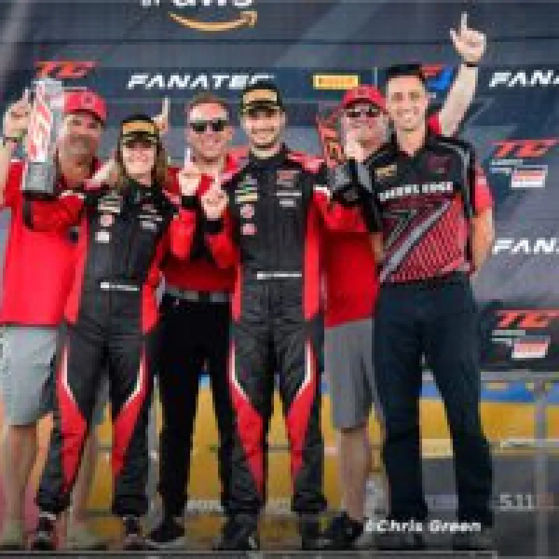 Race car drivers and team celebrate winning with trophy on podium at Fanatec GT Challenge event.
