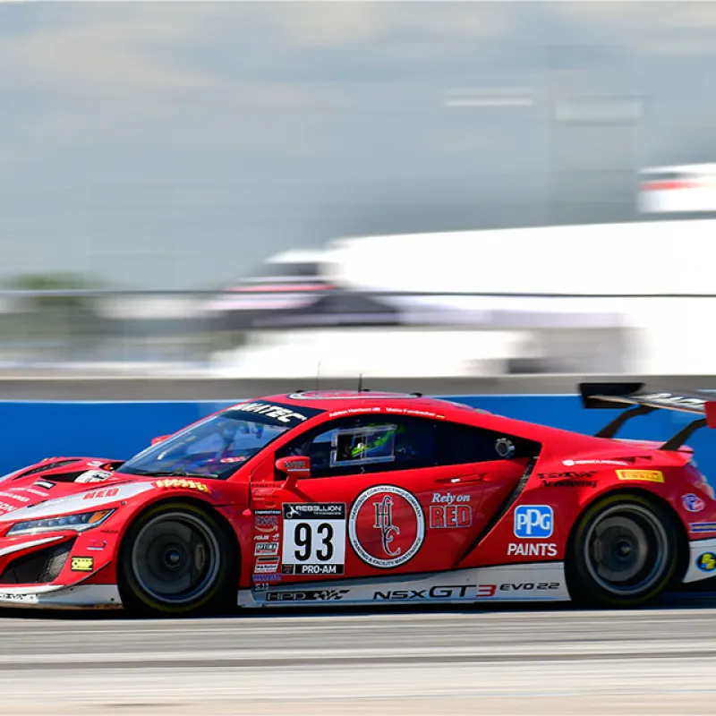 Red Acura NSX GT3 race car number 93 racing on a track with motion blur background.