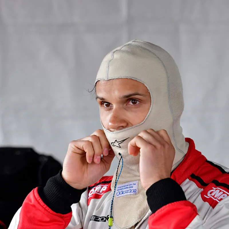 Race car driver in red and white suit adjusting his balaclava before a motorsport event.
