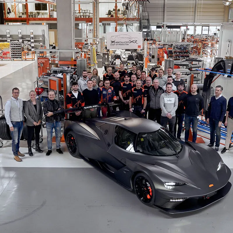 Team of engineers and staff posing with a sleek black high-performance sports car in a spacious factory