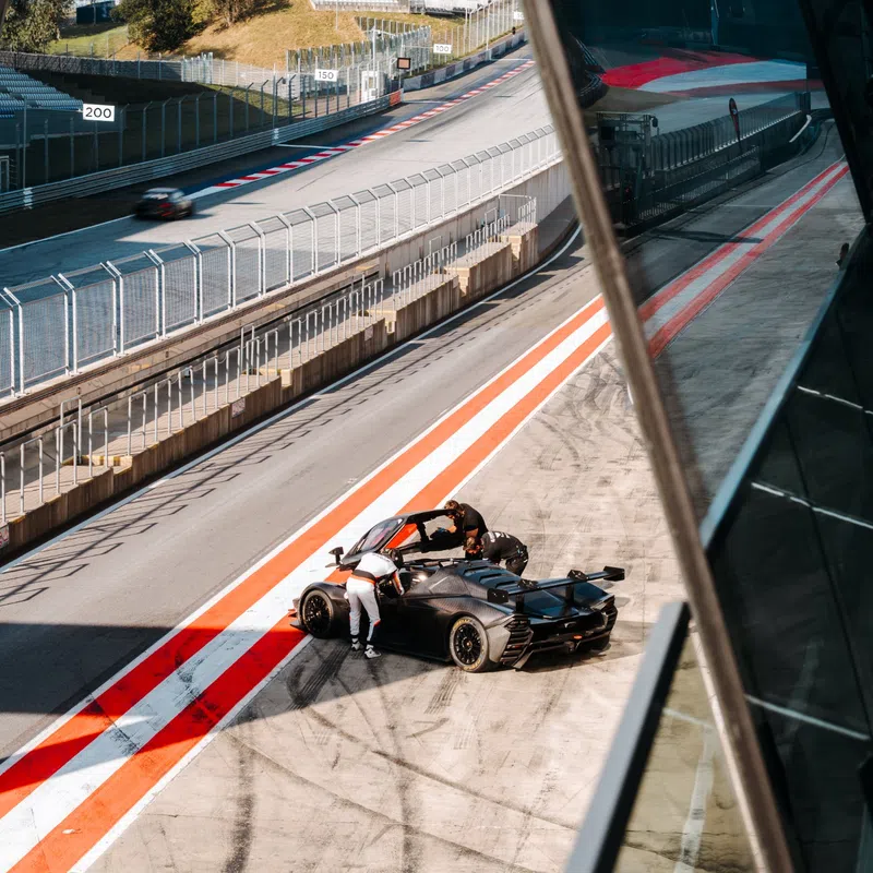 Black race car in pit stop with driver and crew on empty racetrack under clear sky