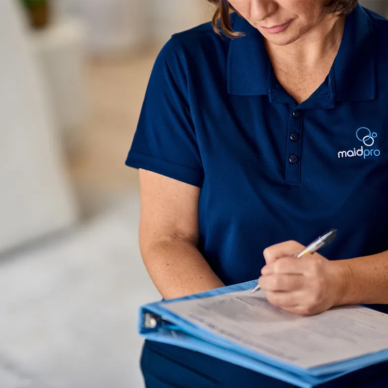 MaidPro cleaning professional in navy shirt filling out checklist on clipboard during service visit.