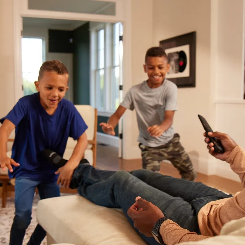 Father relaxing on couch using remote while two boys playfully interact in cozy living room in Downers Grove