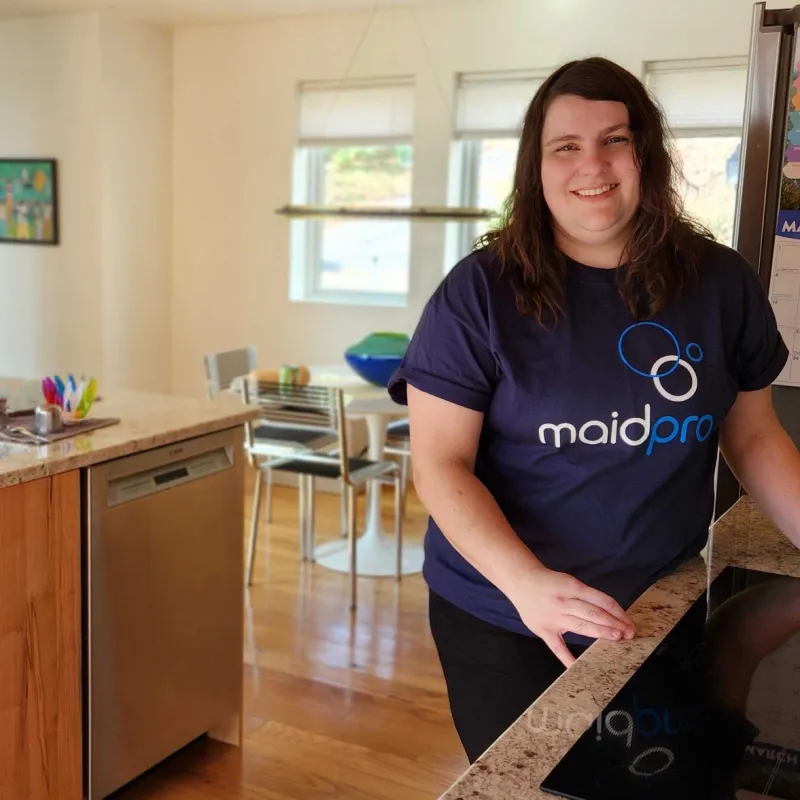Smiling woman in MaidPro shirt in modern kitchen with wooden cabinets and granite countertops