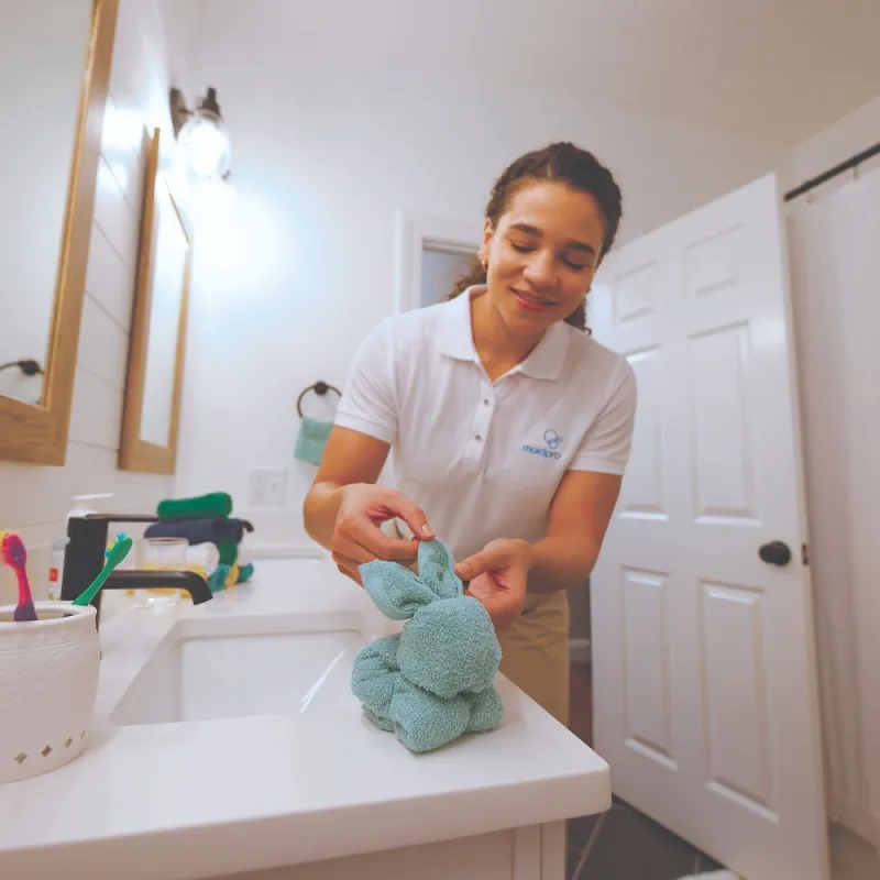 a woman creating a bunny out of a towel in a client's bathroom